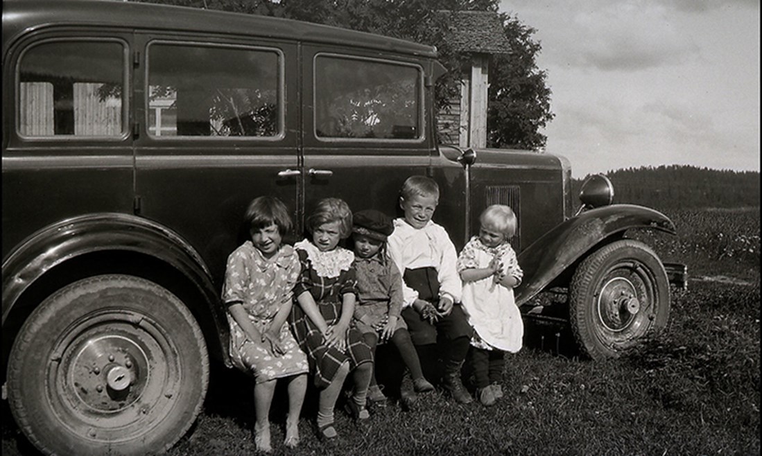 Fem barn som sitter på fotstödet på en bil av märket Buick 1930-tal.