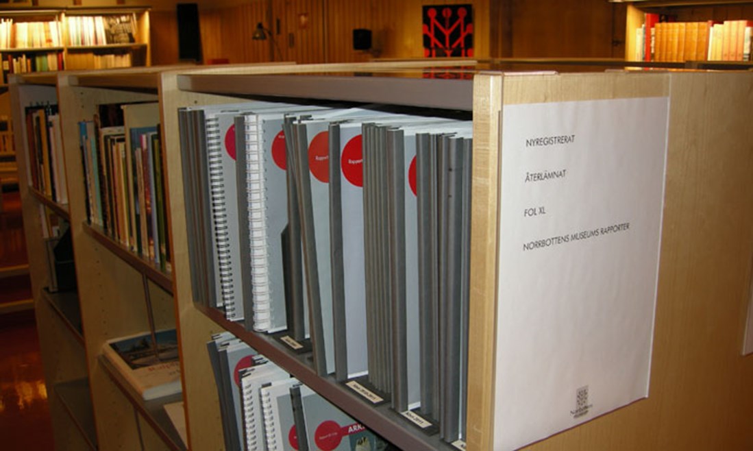 I Norrbottens museums bibliotek i nära anslutning till Norrbotens museums arkiv finns inbundna rapporter att läsa för alla som är intresserade. Fotofrafi på rapporter i hylla i biblioteket.